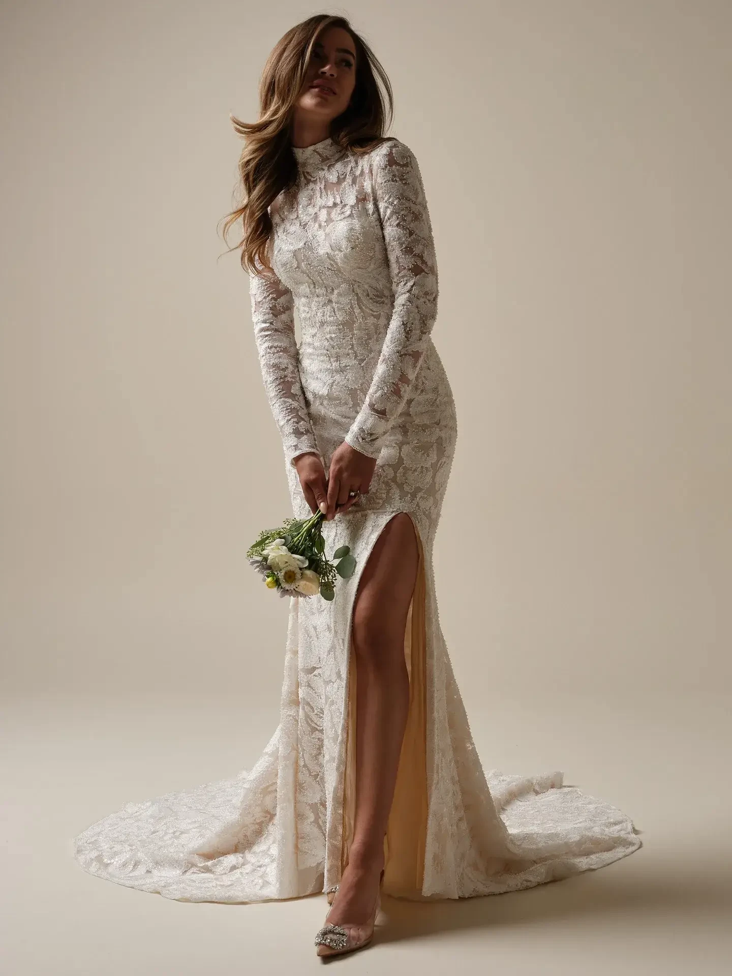 Model is wearing a long sleeve sheath lace wedding dress with a high neckline and slit