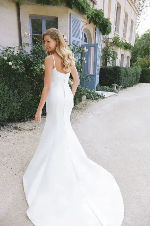 Model is wearing a fit-and-flare gown with a scoop neckline, spaghetti straps, and chapel-length train adorned with lace appliqués.