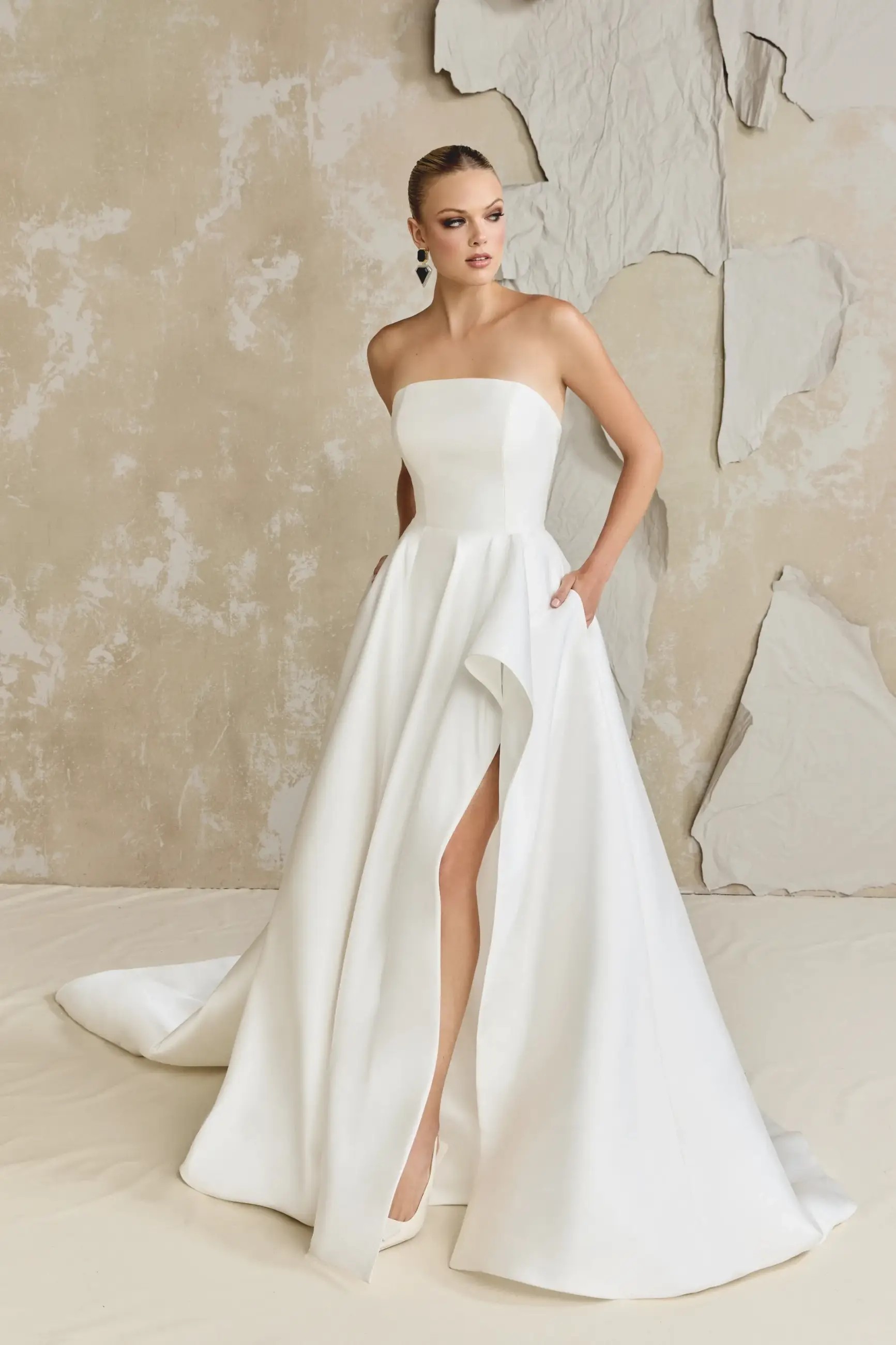 model is wearing a strapless a-line wedding dress with a slit