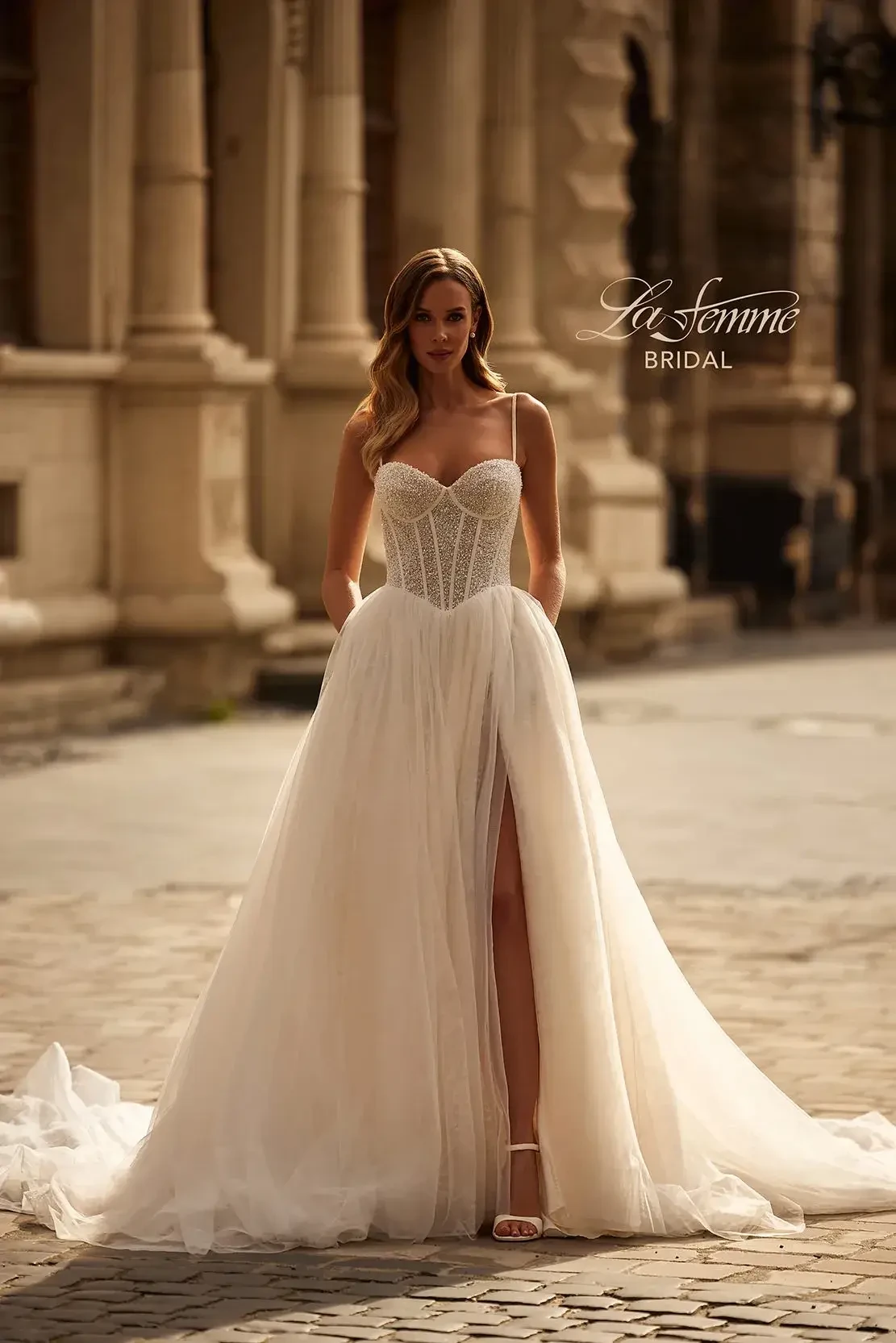 Model is wearing a sleeveless a-line wedding dress with spaghetti straps, a high slit, and structured bodice