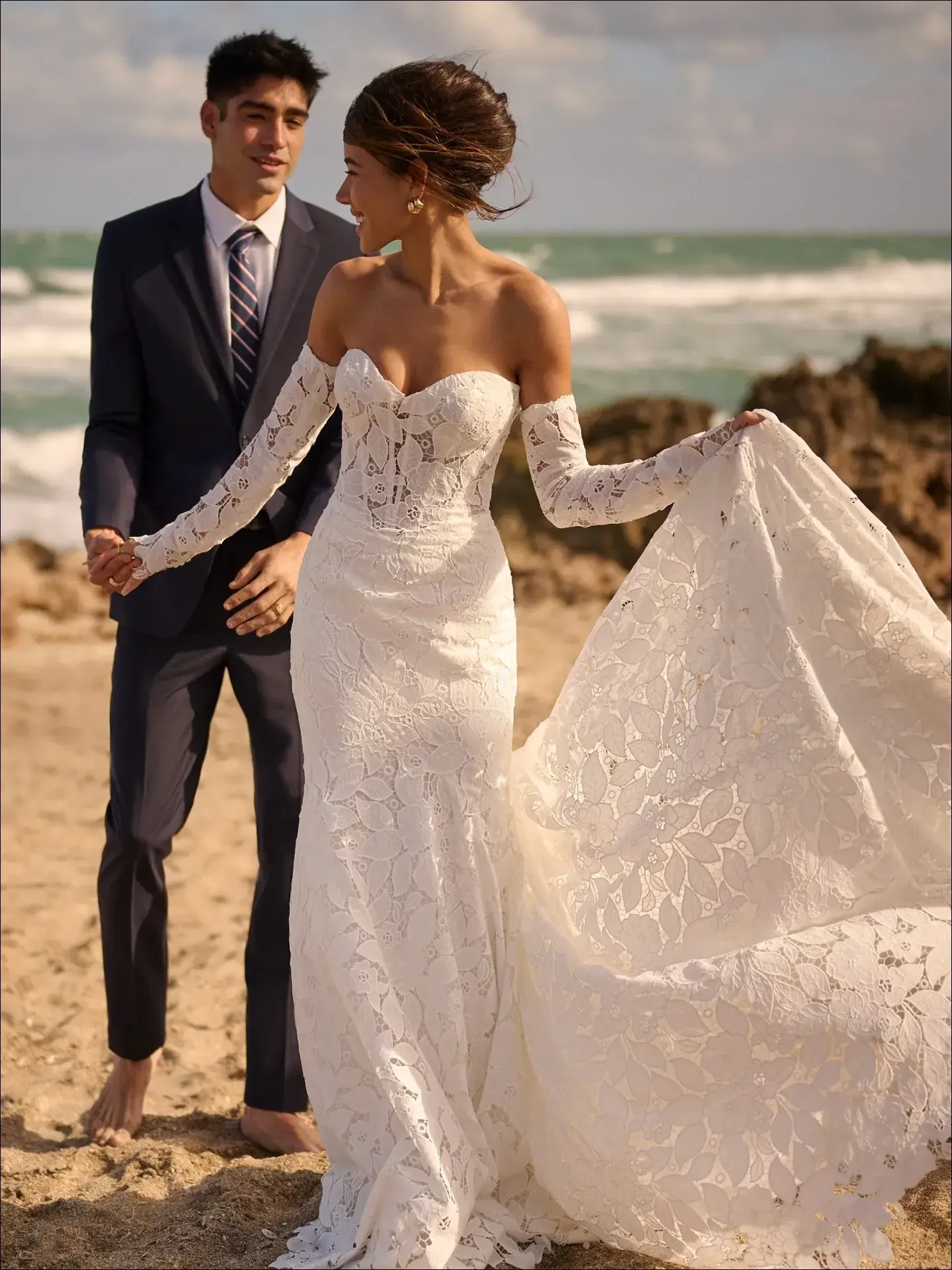 model is wearing a strapless lace fit and flare bridal gown with gauntlet sleeves