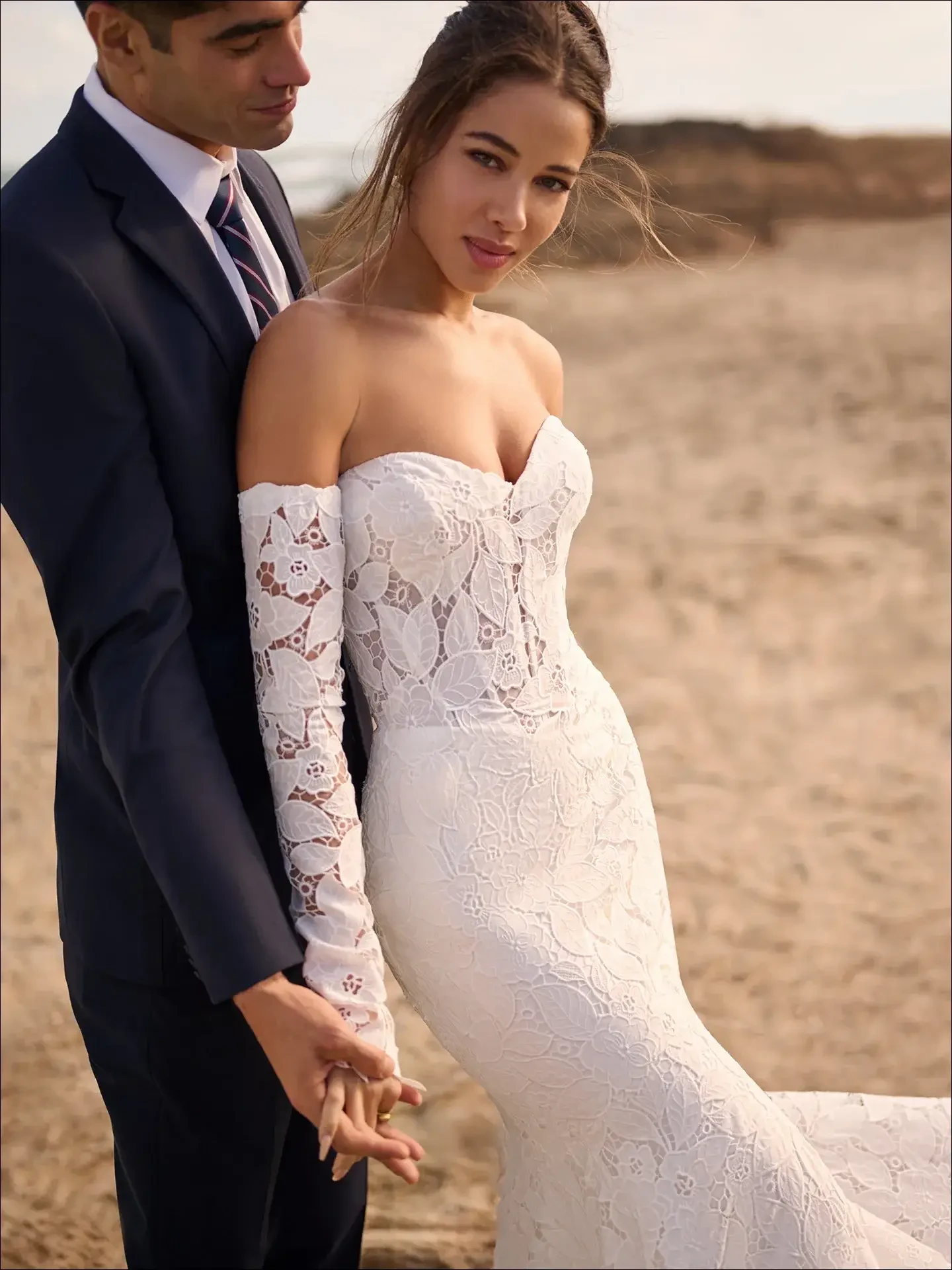model is wearing a strapless lace fit and flare bridal gown with gauntlet sleeves