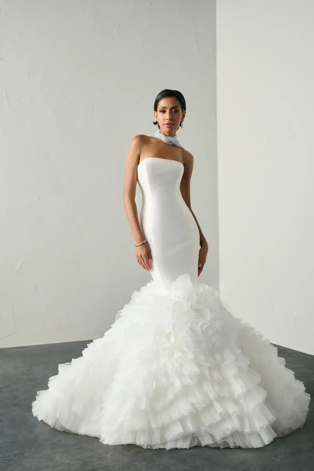 A woman wearing a strapless, mermaid-style wedding dress with a ruffled train.