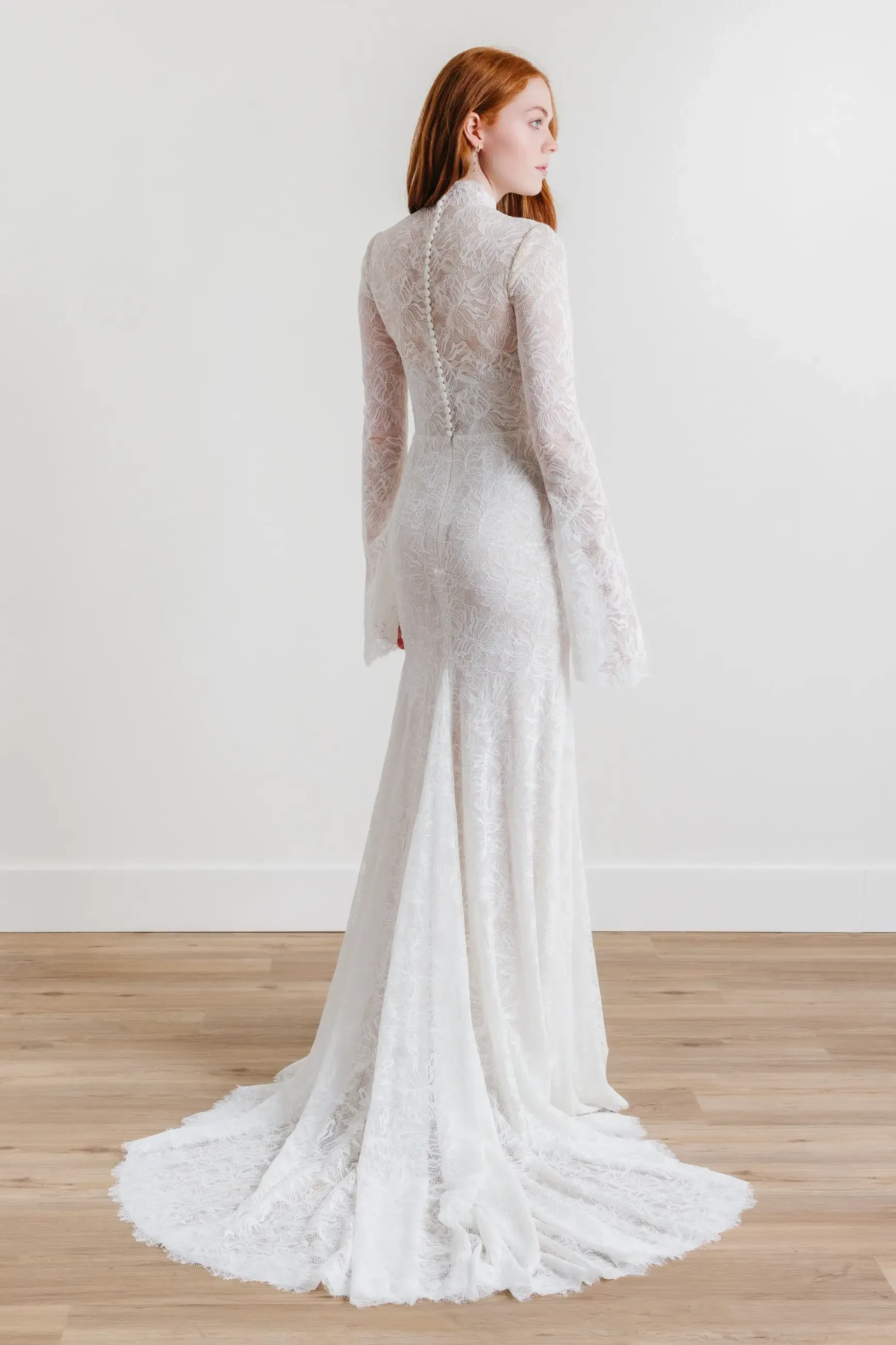 Model is wearing a sheath gown in English net and stretch lace, featuring a high neckline, long sleeves, and a natural waistline.
