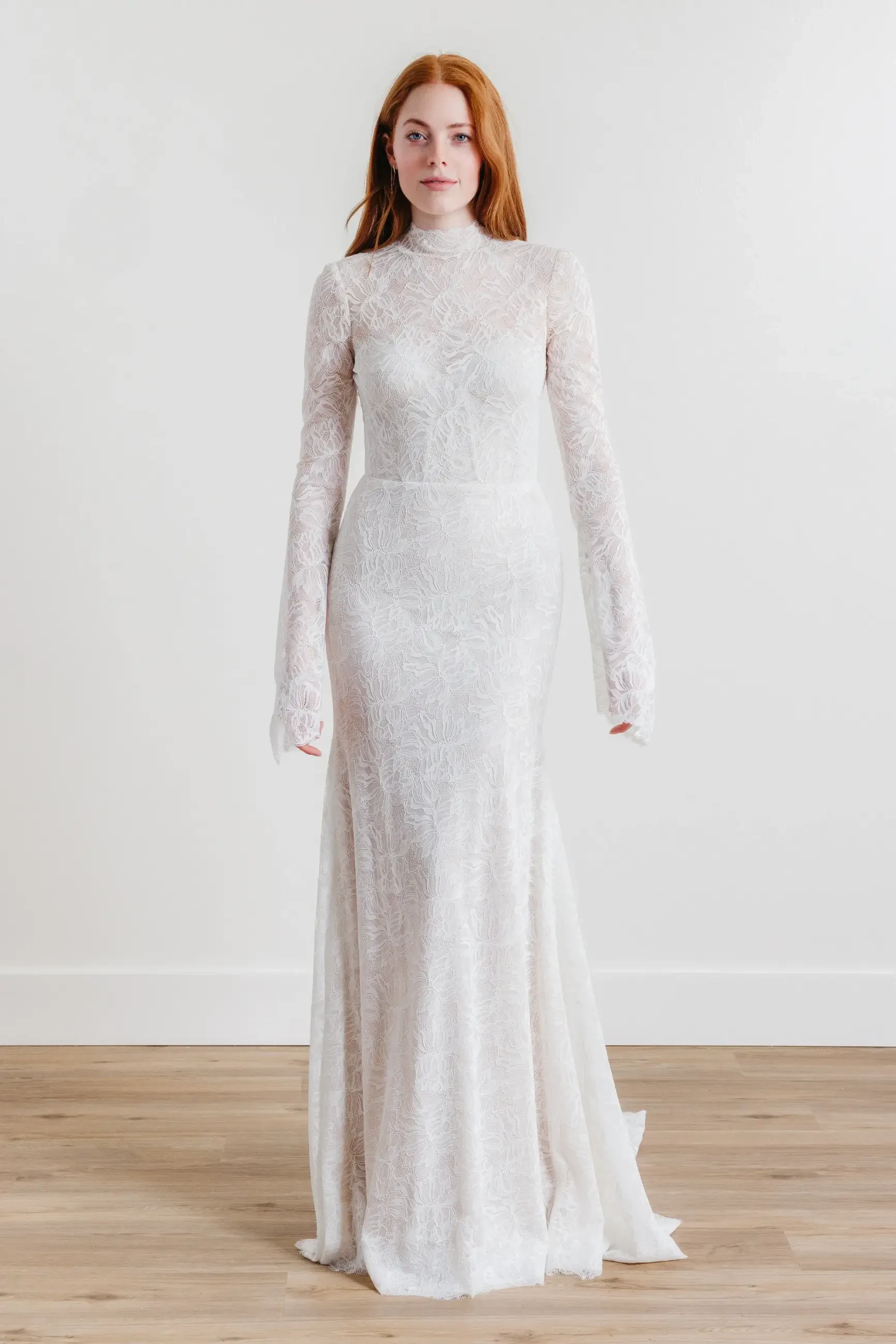 Model is wearing a sheath gown in English net and stretch lace, featuring a high neckline, long sleeves, and a natural waistline.