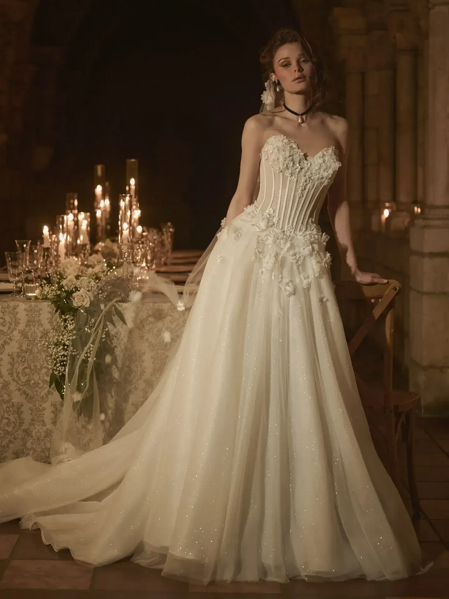 Model is wearing a ballgown with a strapless sweetheart neckline, sheer beaded bodice, and tiered tulle skirt.