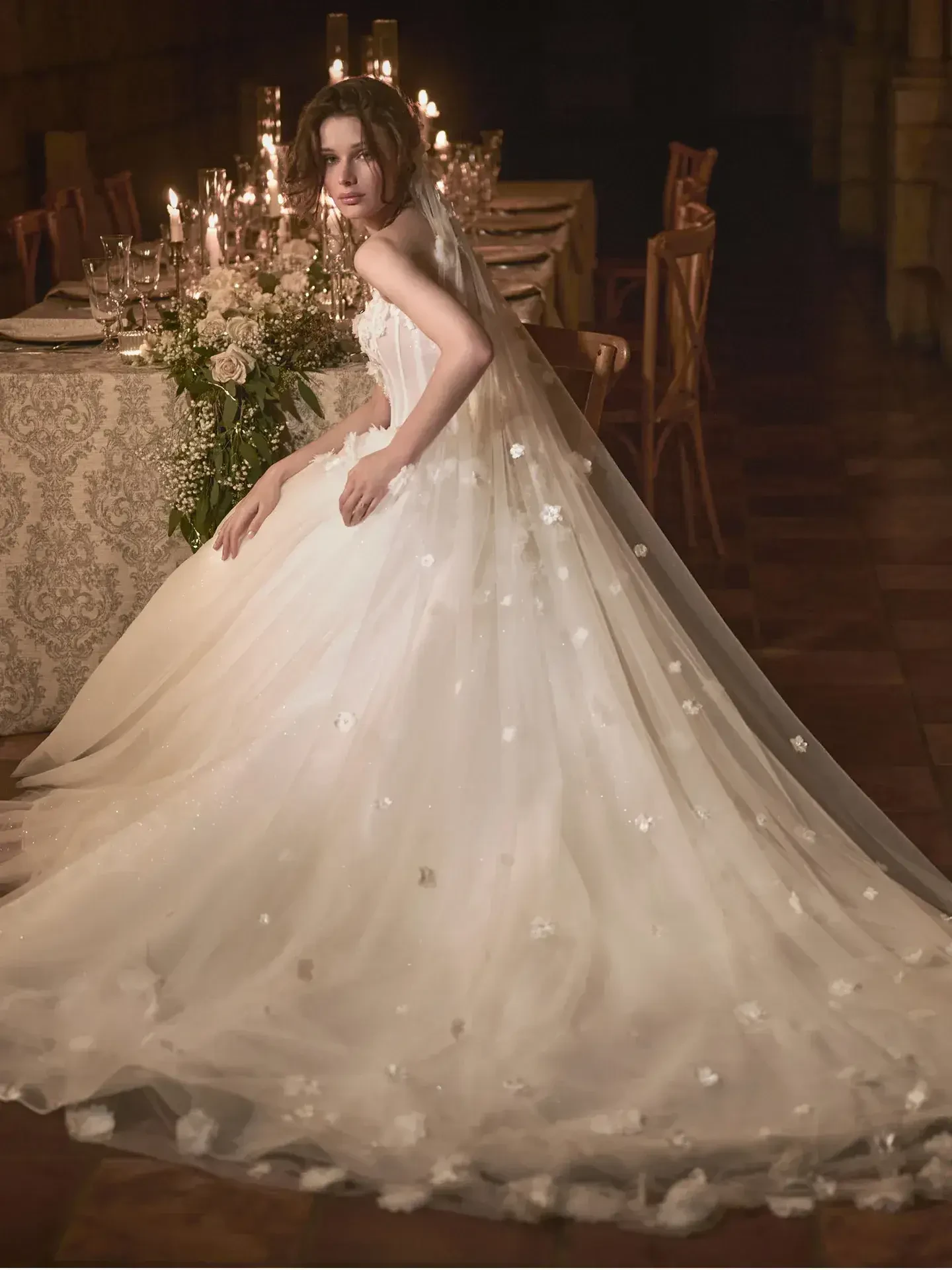 Model is wearing a ballgown with a strapless sweetheart neckline, sheer beaded bodice, and tiered tulle skirt.